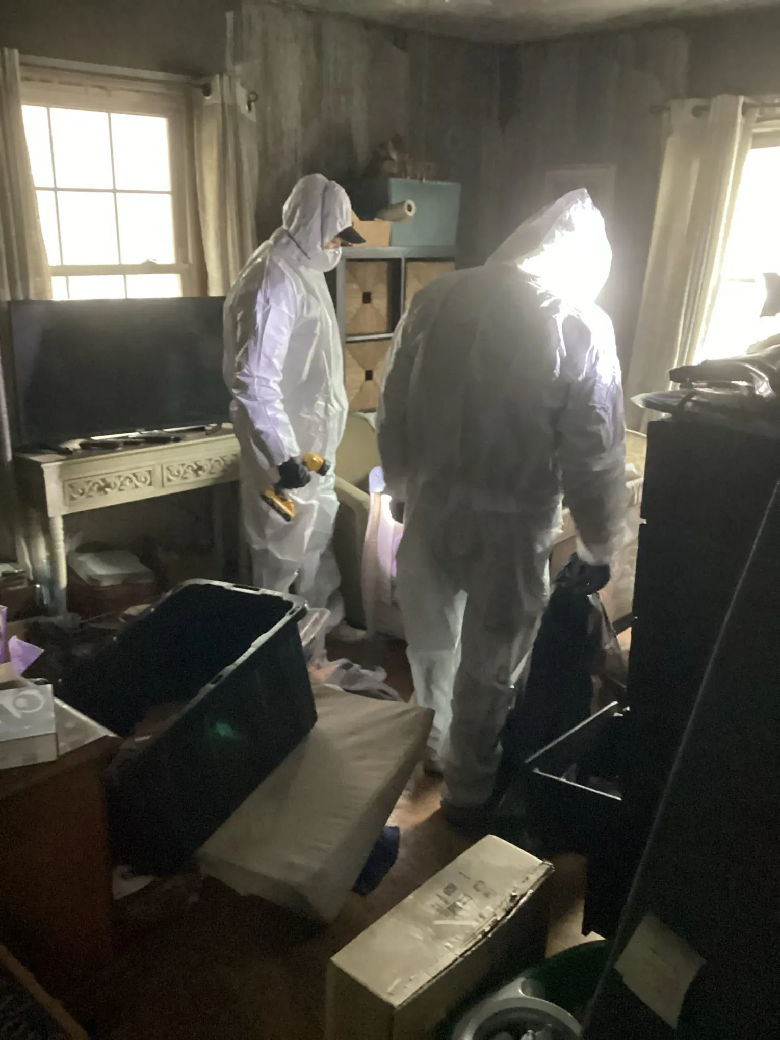 Two technicians in white protective coveralls clearing a fire damaged kitchen into waste bins