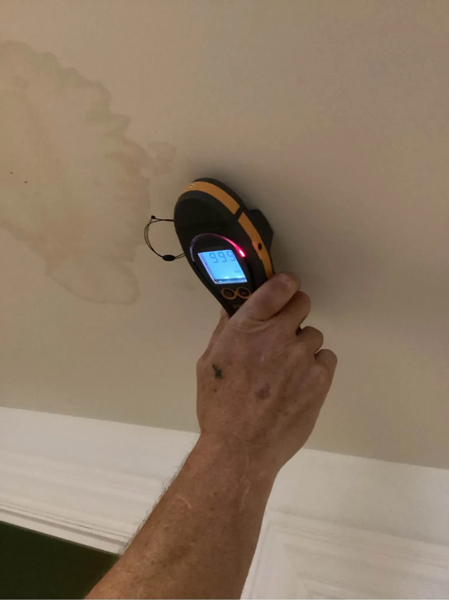 Technician holding a moisture meter against a stained ceiling to confirm a hidden leak