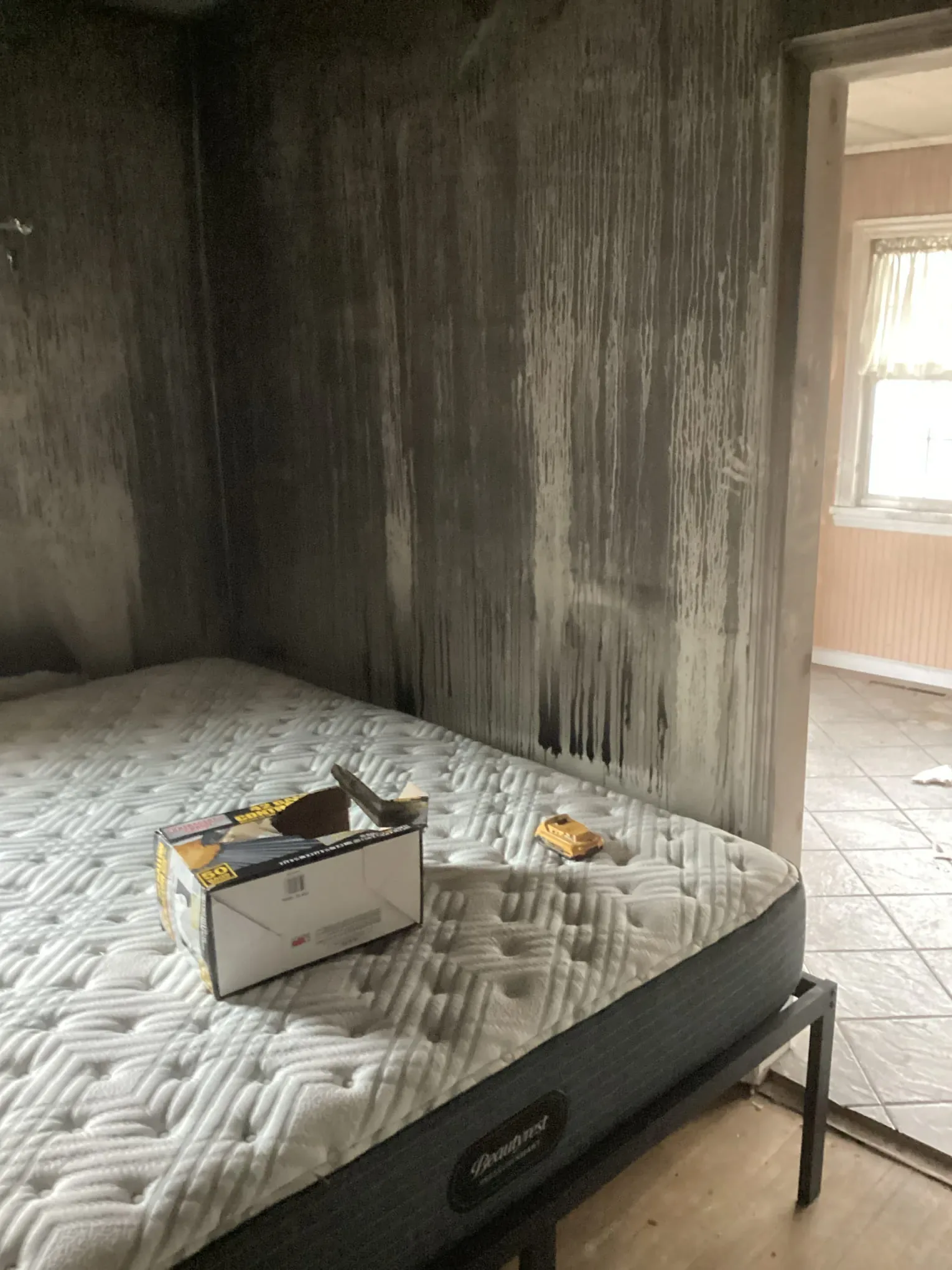 Bedroom with soot covering the walls and a bare mattress left on the frame after a fire