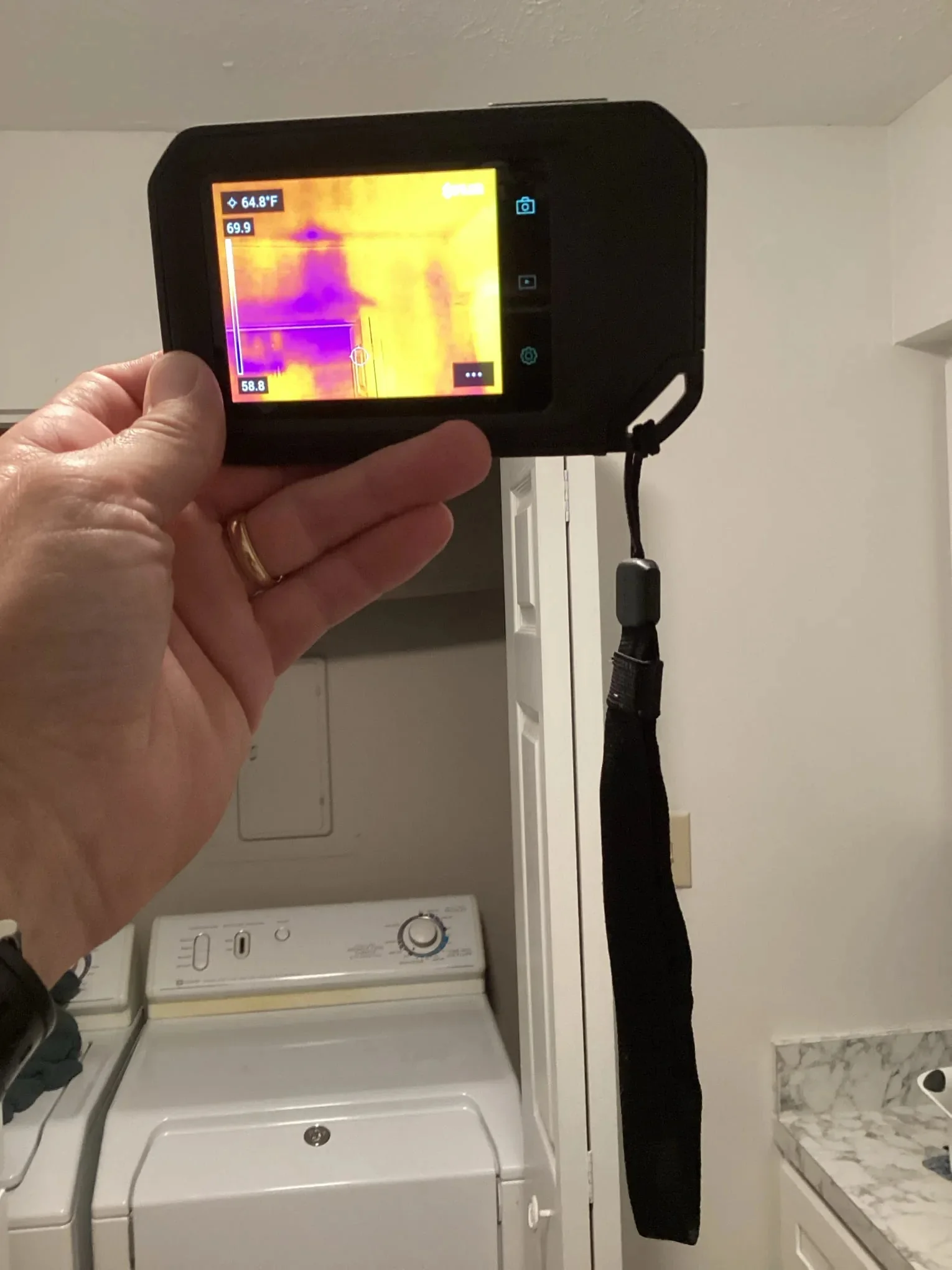 Technician holding a thermal imaging camera against a wall to find moisture behind the surface